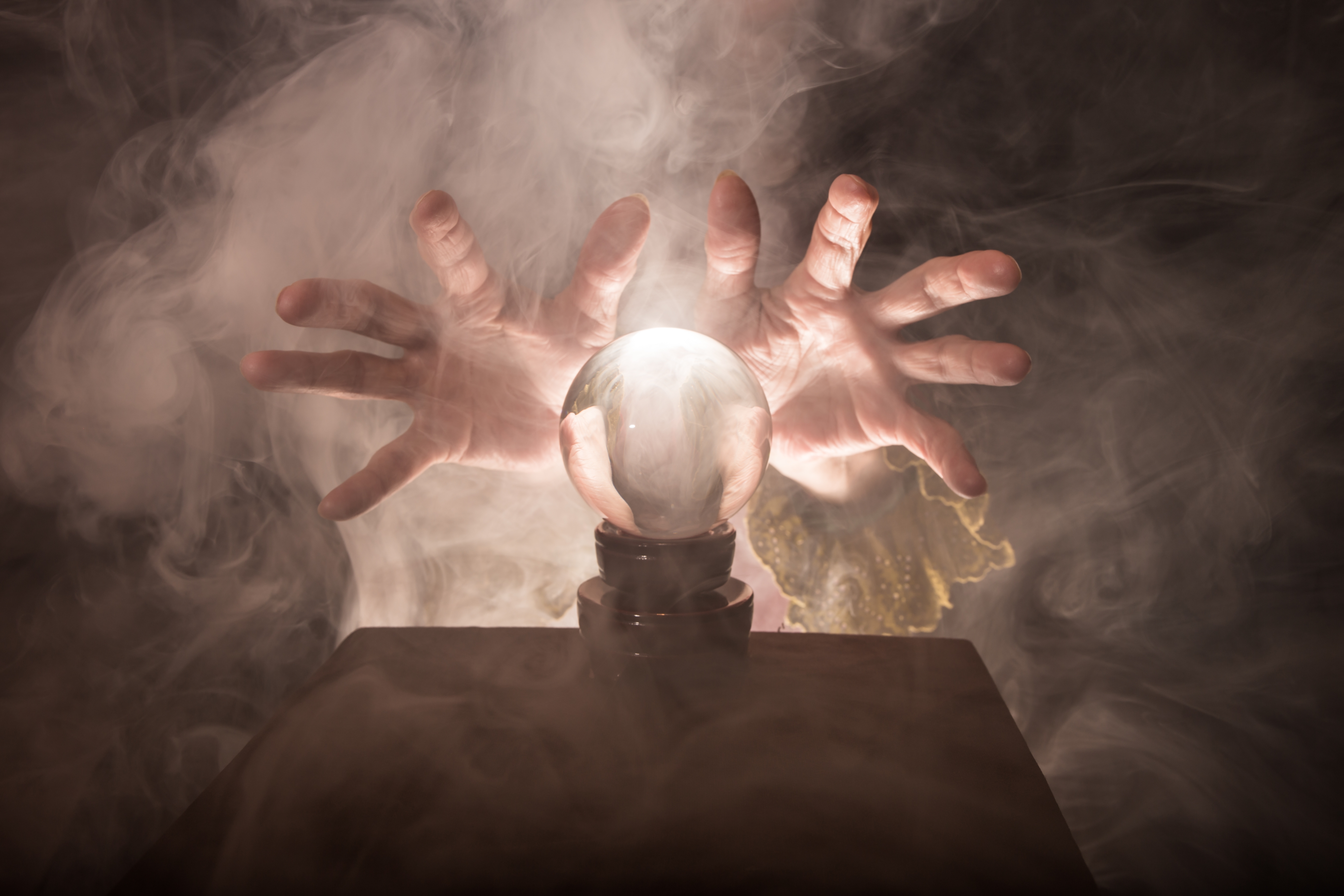 Someone holding their hands above a crystal ball in a smoky room.
