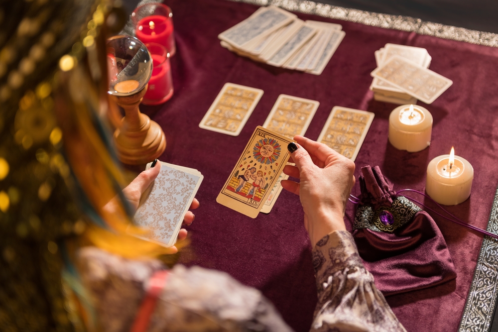 Fortune teller picking sun tarot card while sitting at a table with burning candles and crystals.