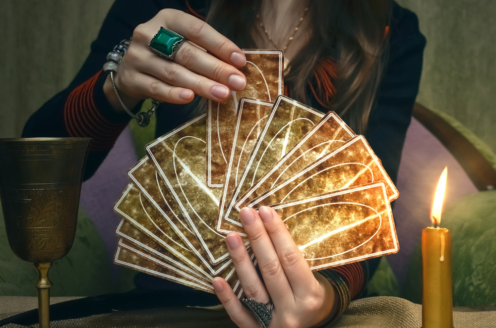 A woman fortune teller holding a deck of tarot cards in her hands begins to shuffle it.