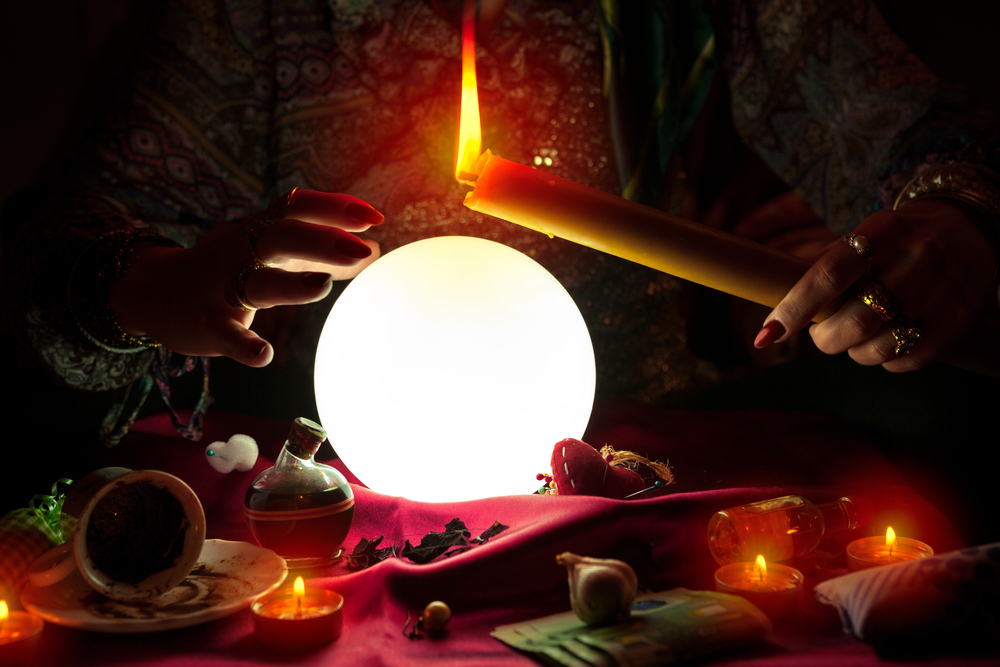 Fortune teller woman holding candle above a glowing crystal ball.