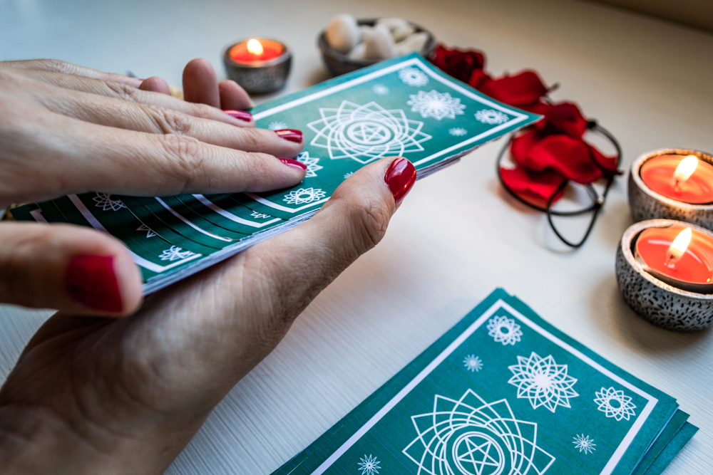 A fortune reader with green tarot cards on a white wooden table background. Concept of divination.