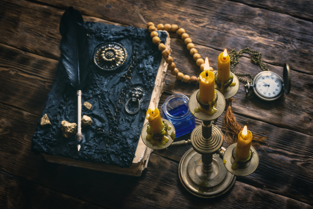 Ancient magic book, pocket watch and a black quill pen in the light of a burning candle on a wooden table background.