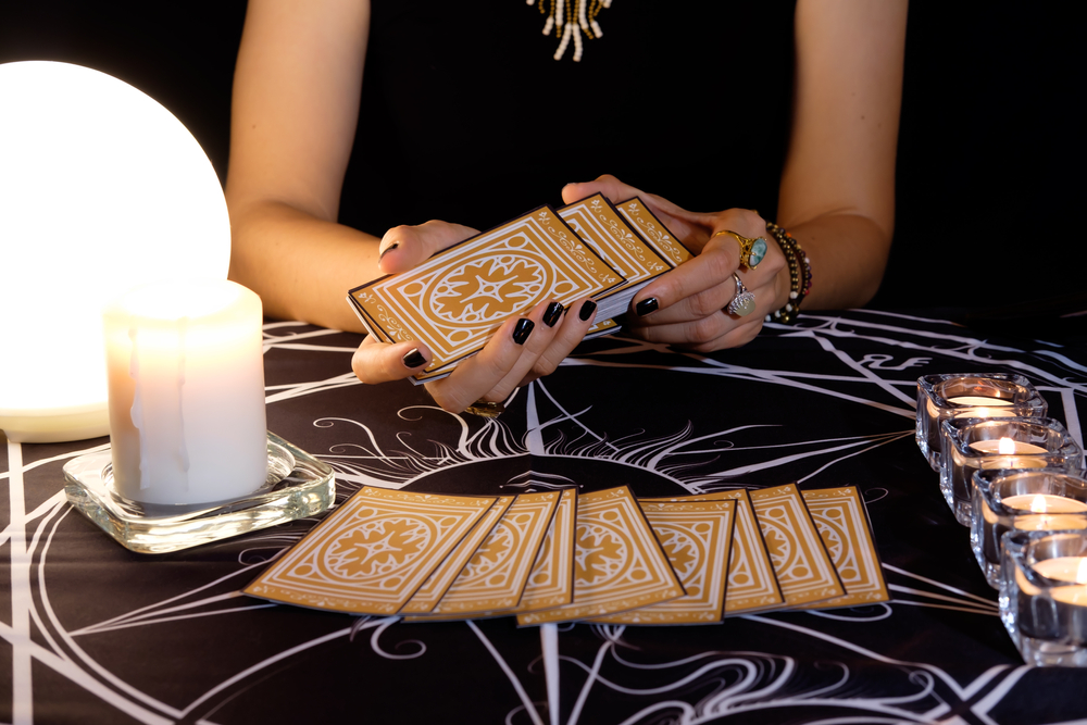 Fortune reader shuffling cards in her hands. Tarot cards face down on a table near a crystal ball and burning candles.